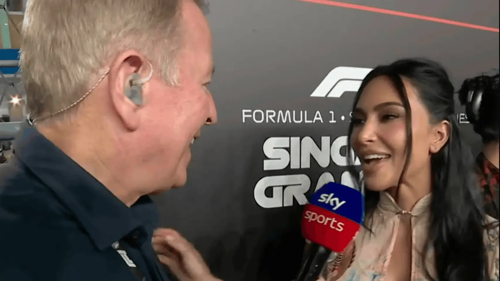 Martin Brundle holding his microphone towards Kim Kardashian on the Singapore grid at night
